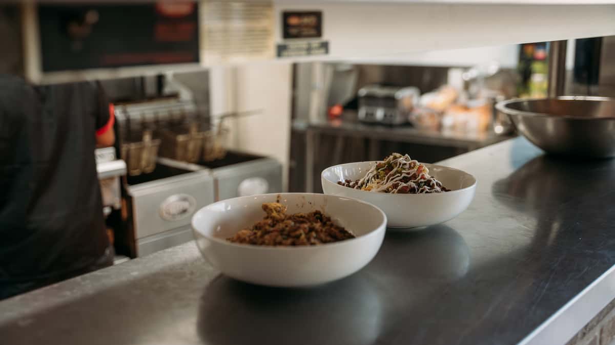 Two freshly prepared bowls of hearty meat and veggie dishes, one topped with creamy sauce, ready to be served from the kitchen line.