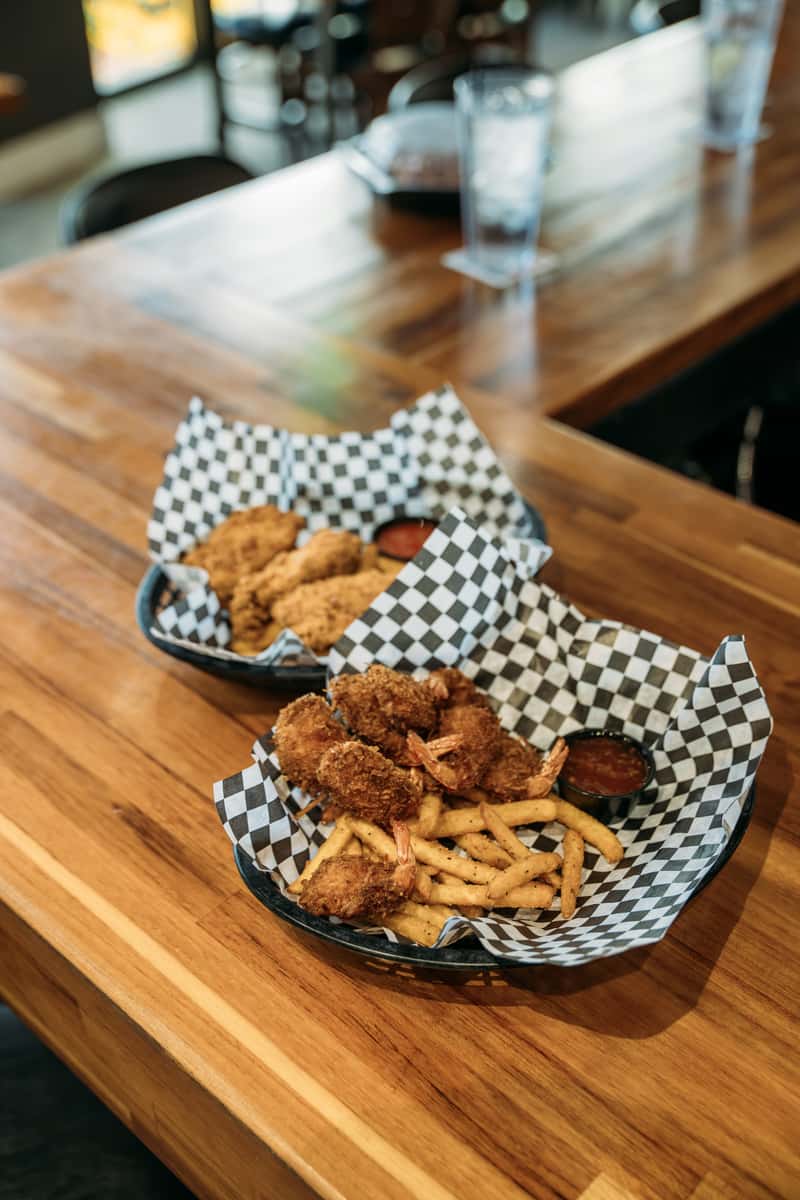 Crispy fried shrimp and golden French fries served in a basket with tangy dipping sauce, perfect for a hearty seafood meal.