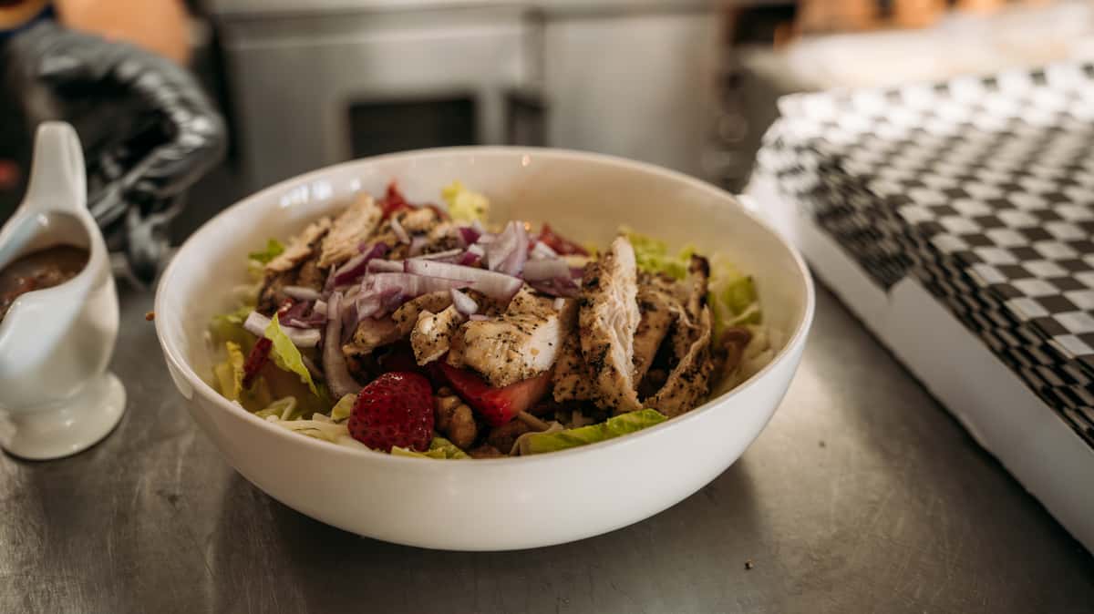 Fresh grilled chicken salad with mixed greens, red onions, strawberries, and walnuts, served with a side of balsamic dressing.