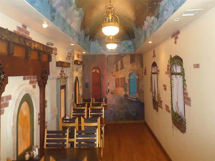 Dining area in corridor with Italian-style village paintings on walls.