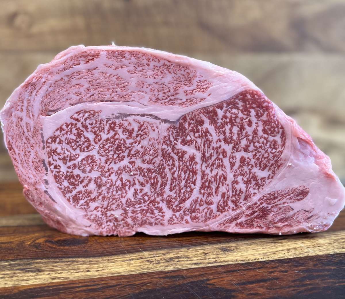 A raw Wagyu beef steak with intricate intramuscular fat marbling rests on a wooden cutting board, showcasing the rich texture of premium Wagyu beef.