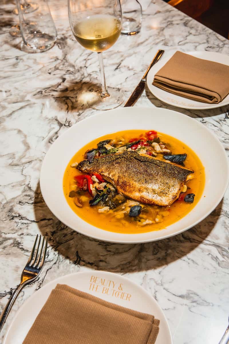 Chef-driven steakhouse fish entrée served with vegetables and sauce.