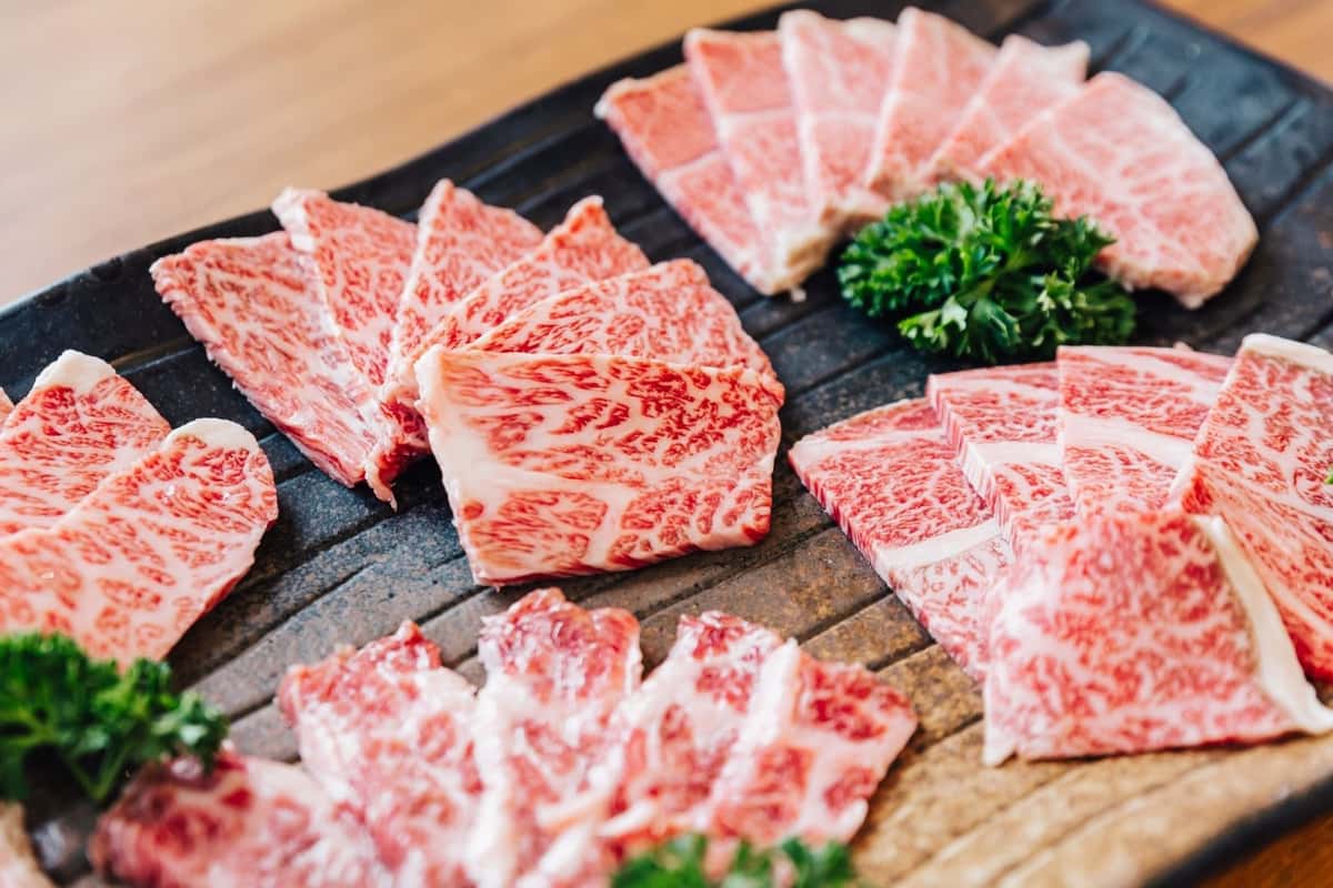 Thin slices of raw A5 Wagyu beef with rich intramuscular fat marbling are arranged on a black serving platter and garnished with fresh parsley.