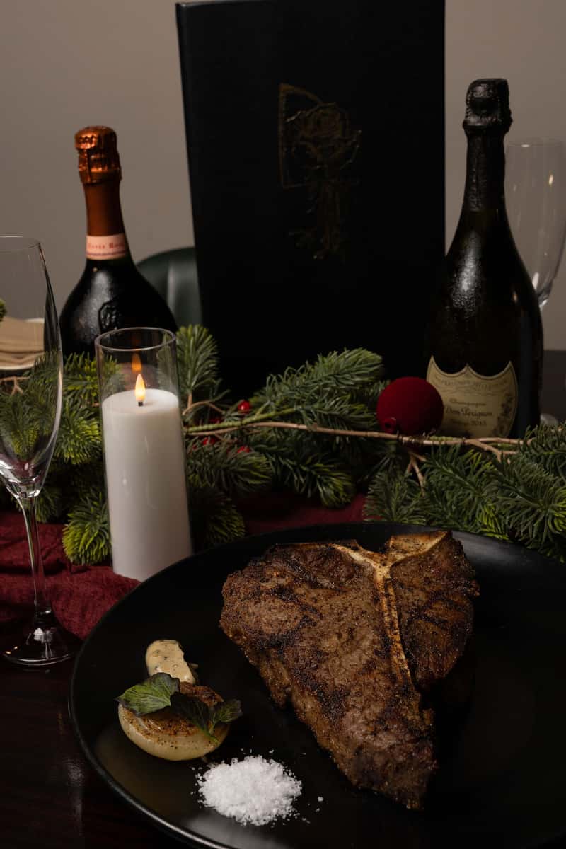 Bone-in grilled steak presented in an upscale modern steakhouse setting with candles and wine.