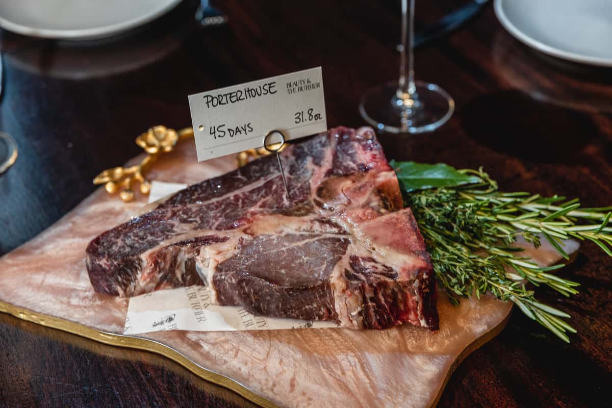 Raw 45-day dry-aged porterhouse steak displayed with fresh herbs.