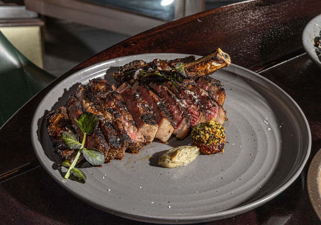 Sliced dry-aged cowboy chop with sauce and herb garnish.