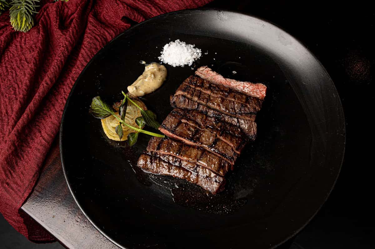 Sliced grilled steak plated with sea salt, sauce, and roasted onion at a modern steakhouse.