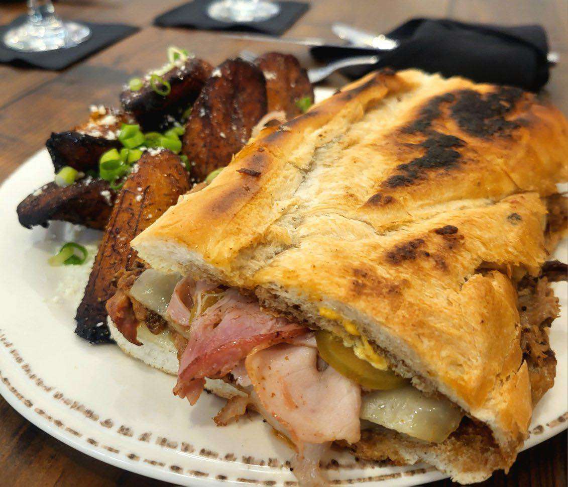 Pressed Cuban sandwich filled with ham, pork, pickles, and cheese, served with crispy plantains topped with green onions and cheese.