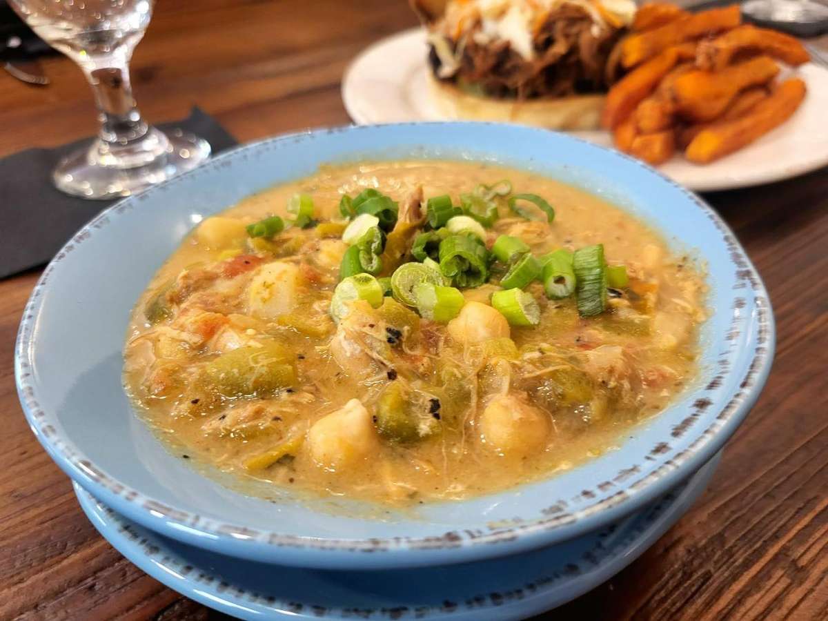 Hearty chicken and vegetable stew featuring chickpeas, green beans, and potatoes, topped with fresh green onions and served in a rustic blue bowl.