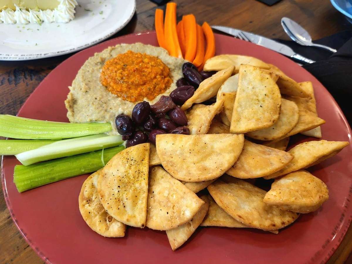 Appetizer plate with fried pita chips, kalamata olives, celery, carrots, and creamy dip topped with red pepper spread.