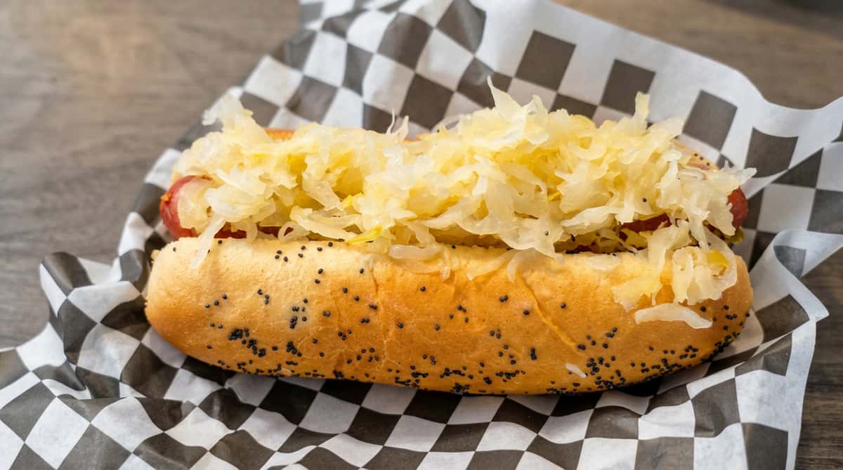 Hot dog in a poppy seed bun topped with sauerkraut, on checkered paper.
