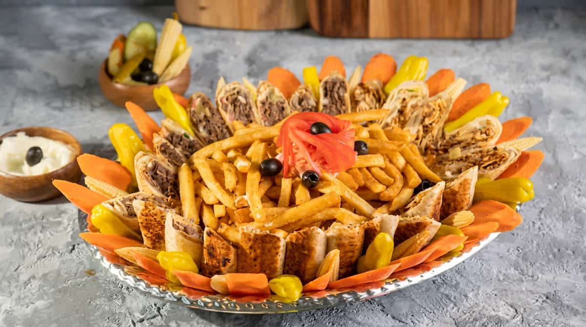 Shawarma platter with fries, sliced tomato, olives, pickled carrots, and peppers.
