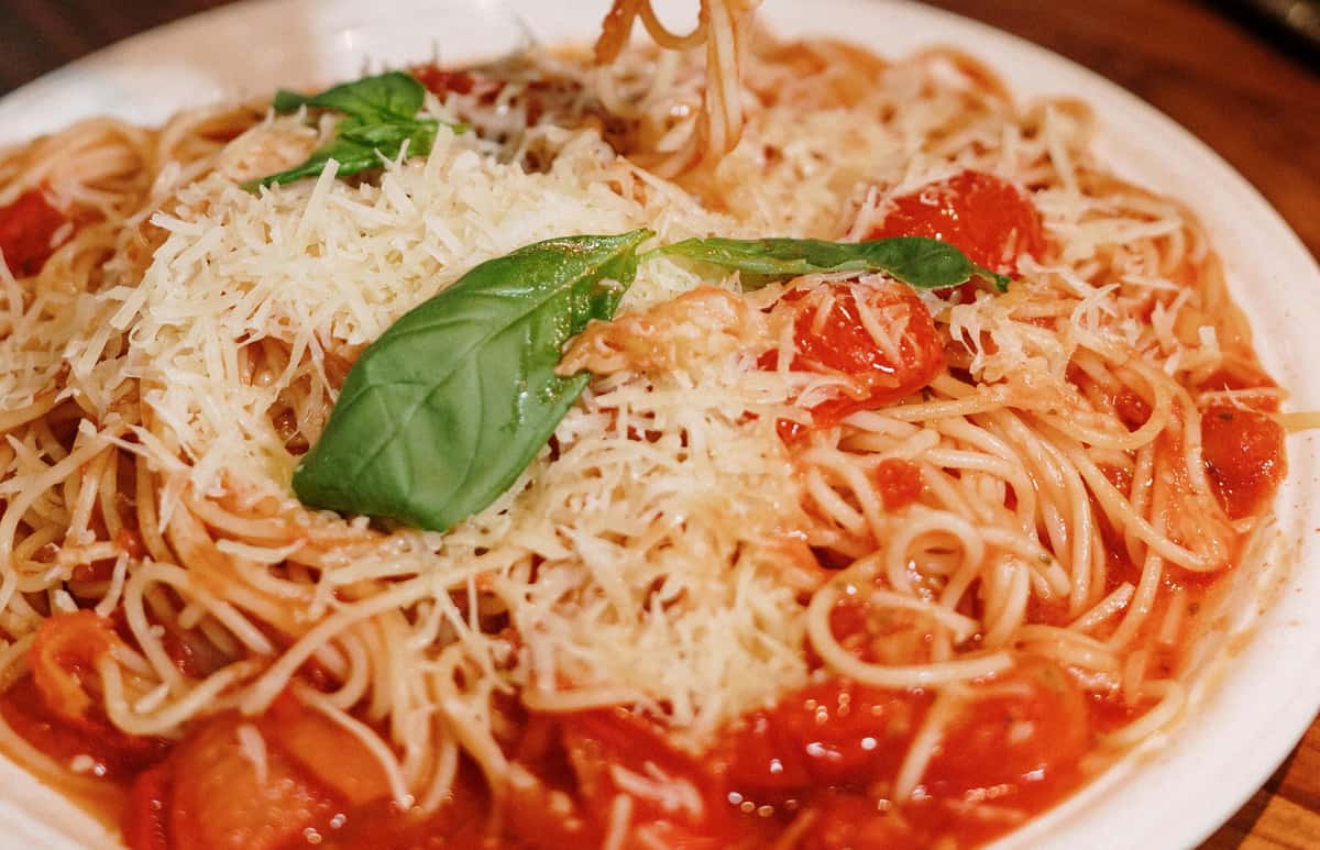 Spaghetti with marinara sauce, grated parmesan cheese, cherry tomatoes, and fresh basil leaves on a white plate.