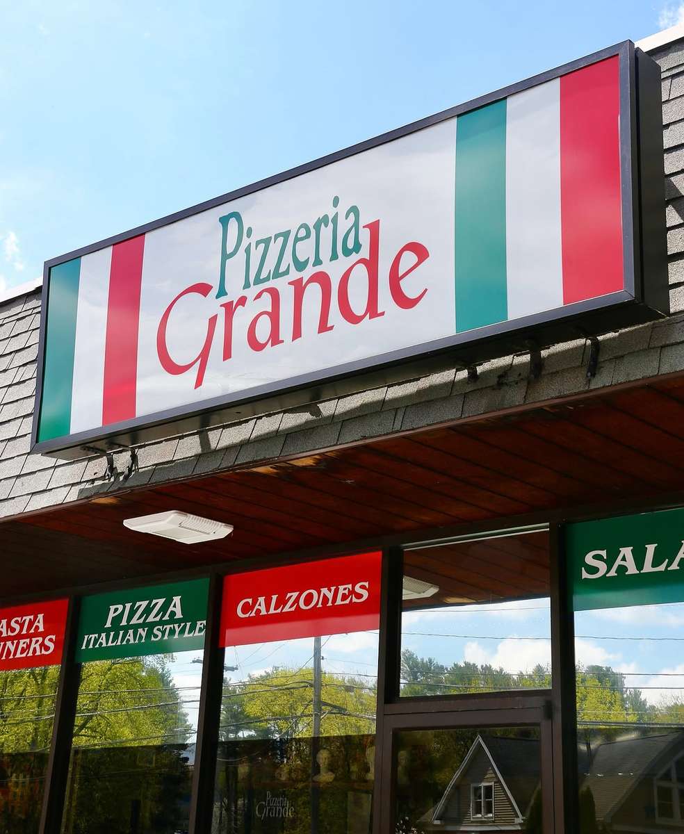 Pizzeria Grande storefront with Italian flag-themed sign and window banners highlighting pizza, calzones, pasta, and salads.