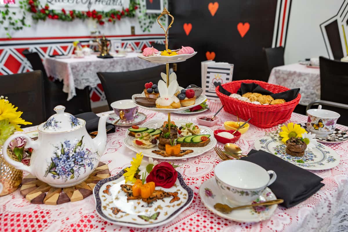 Three-tiered afternoon tea stand with assorted finger sandwiches, bunny-themed sweets, chocolate mousse, and meringues in a Queen of Hearts tea room.