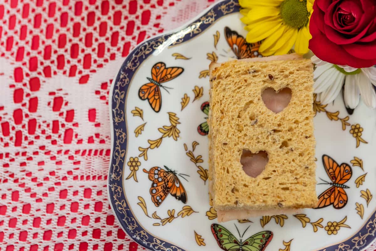 Delicate tea sandwich with sliced turkey and cheese on multigrain bread, served on a butterfly-themed porcelain plate.