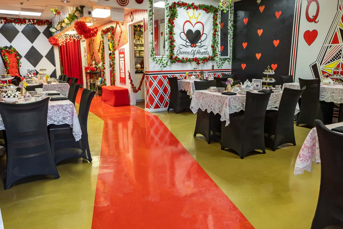 Whimsical Queen of Hearts-themed tea room with red and black card suit decor, lace-covered tables, and vibrant Alice in Wonderland flair.