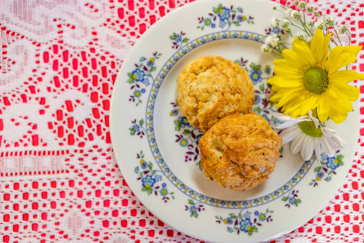 Golden brown tea scones with a crisp exterior, served on a floral china plate with daisy and yellow flower accents.