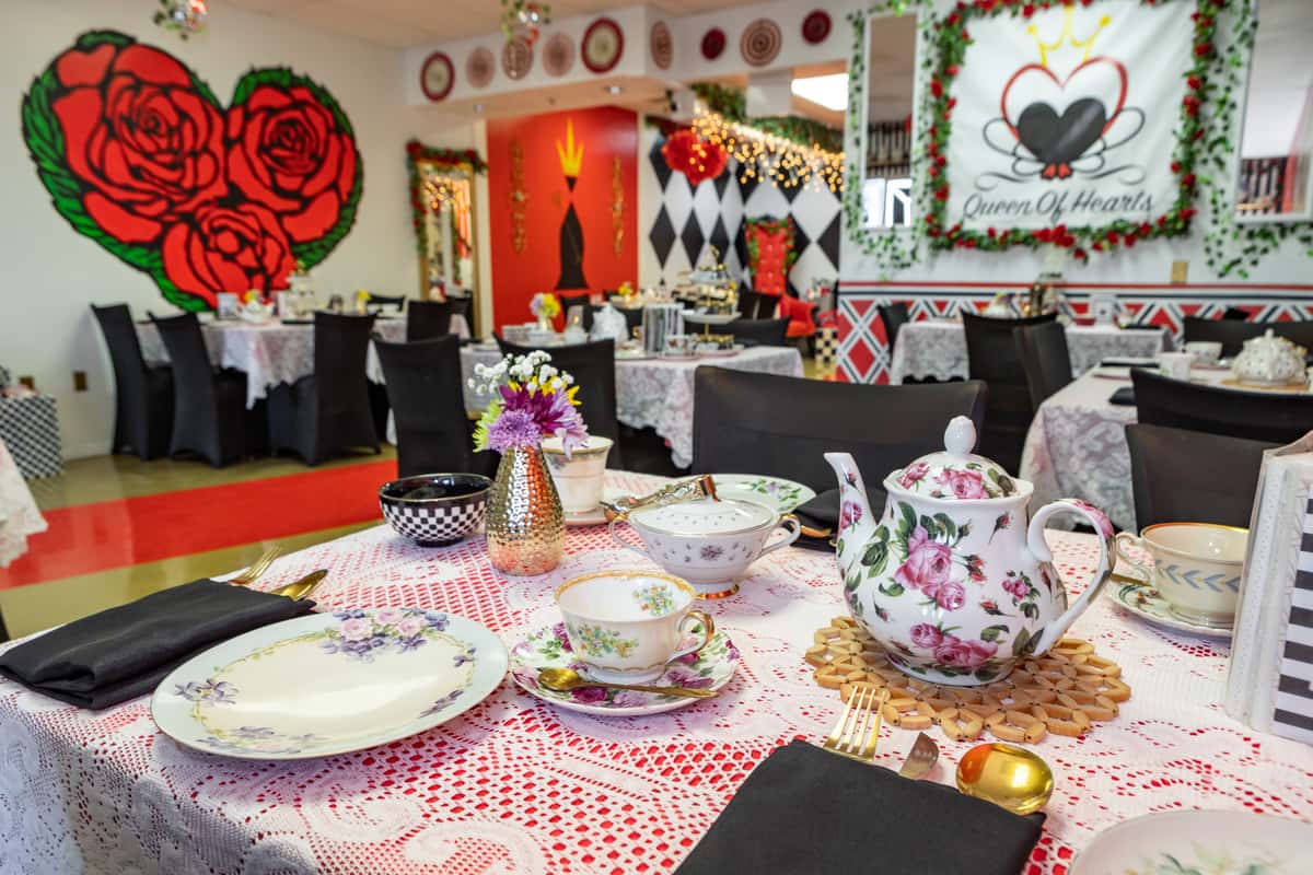 Eclectic Alice in Wonderland tea room with rose-themed decor, floral china, and Queen of Hearts accents for a whimsical dining experience.
