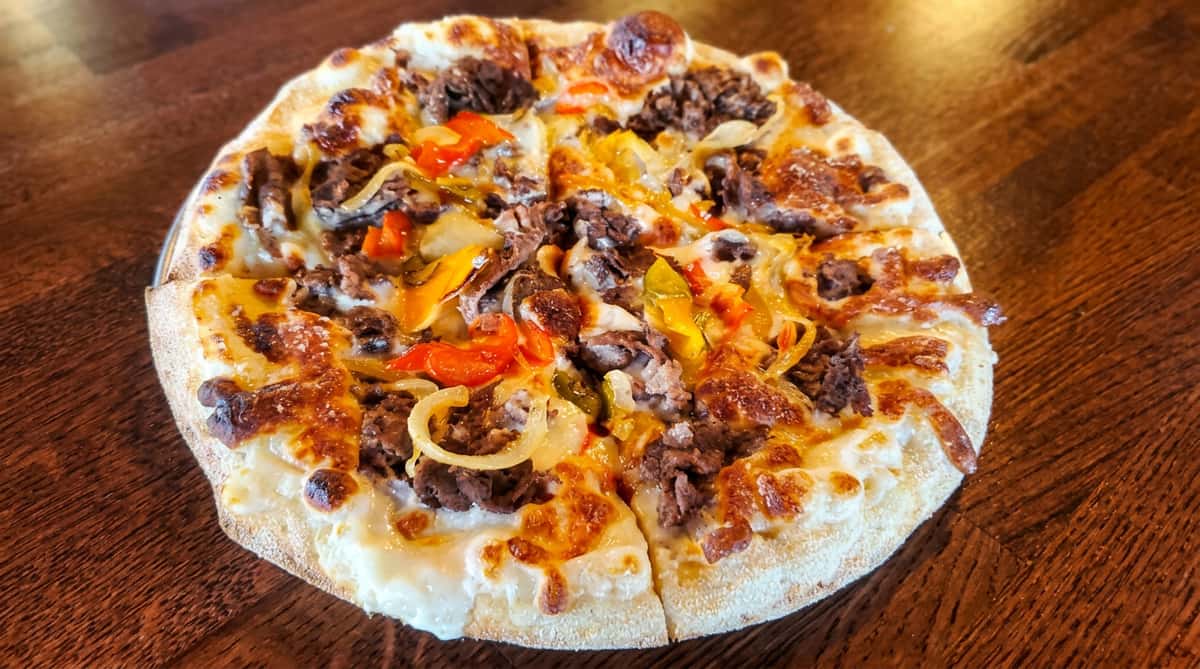Pizza with melted cheese, ground beef, sautéed onions, and colorful bell peppers on a wooden table.