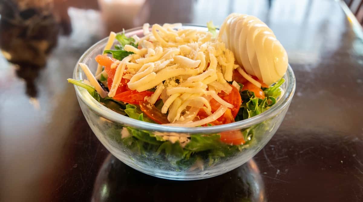 Green salad with lettuce, tomato, shredded cheese, and a sliced hard-boiled egg in a clear bowl.