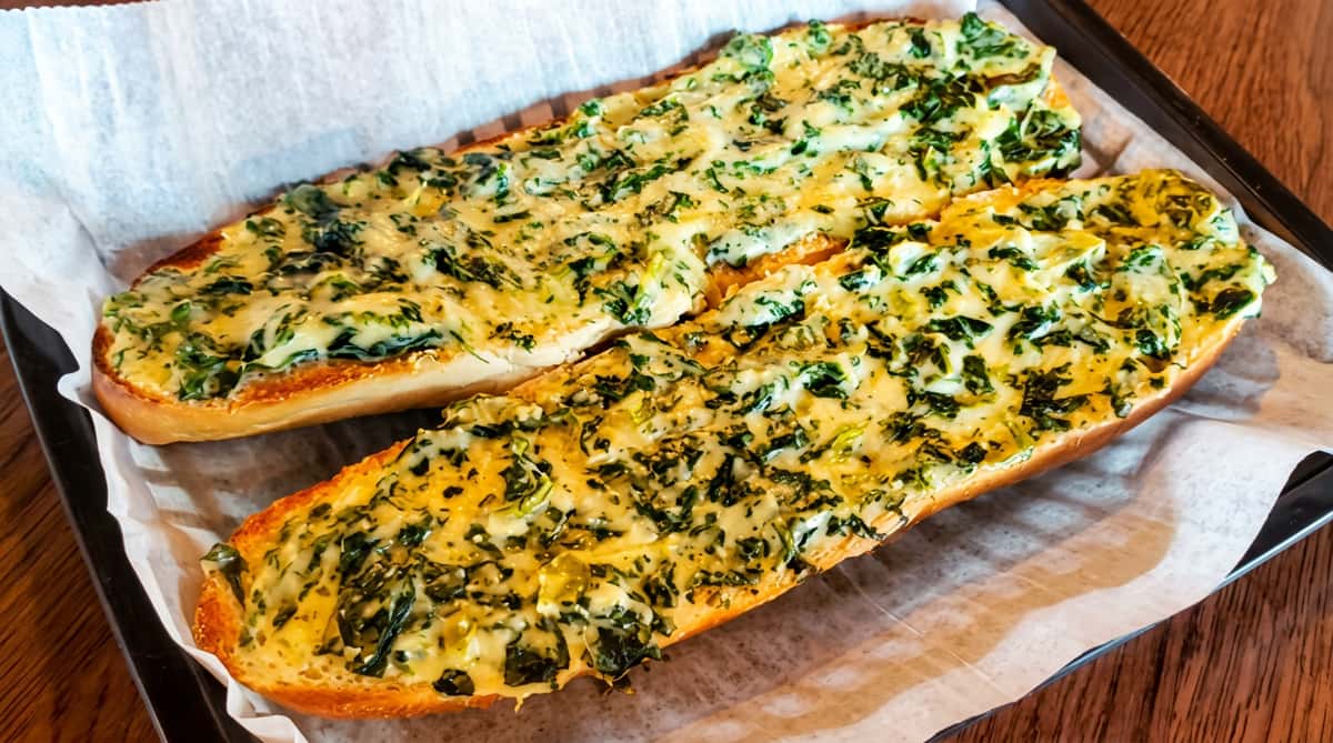 Baked spinach and cheese dip spread on two halves of a toasted baguette, served on parchment paper.