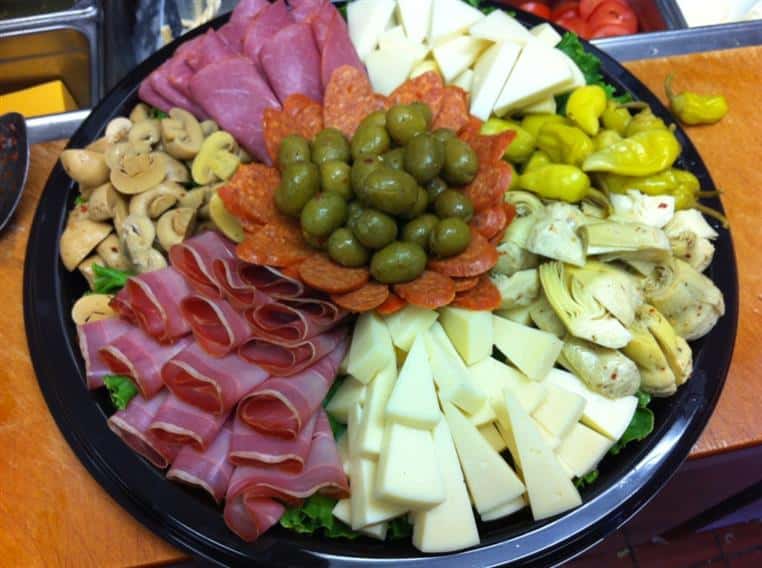 various meats and cheeses on a tray with olives, artichokes, pepperoncini and mushrooms
