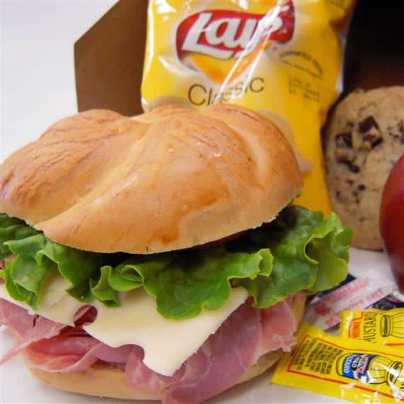 ham and swiss sandwich served on a bun with a side of potato chips and a cookie