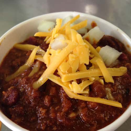 bowl of chili topped with shredded cheese and white onions