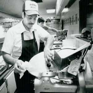 old photo of Augie as the chef in the kitchen using the meat slicer 