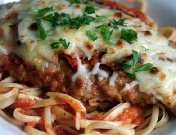 chicken parm with melted mozzarella and parsley as a garnish served over linguine and tomato sauce
