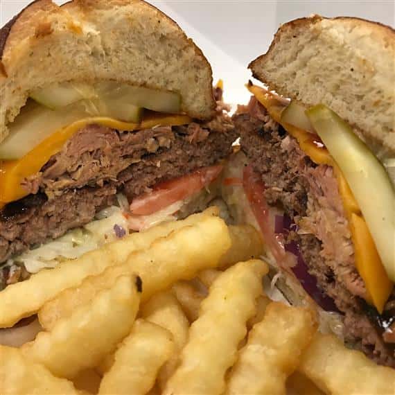 cheeseburger with coleslaw, lettuce, tomato, beef patty, cheddar cheese, and pickles on a toasted bun served with crinkle cut french fries