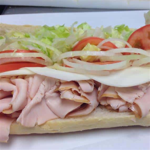 sub sandwich being made with turkey, provolone cheese, onions, shredded lettuce, tomatoes, and mustard