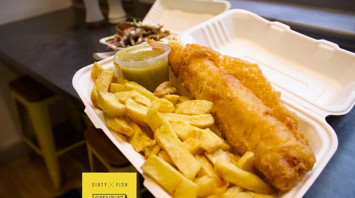 Golden battered fish served with chunky chips and a wedge of lemon in a takeaway box.
