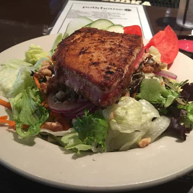 Blackened ahi tuna served over a mixed green salad with walnuts, red onions, tomatoes, and cucumbers.