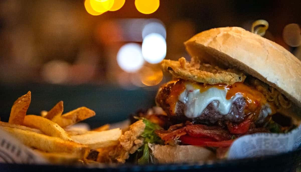 Juicy cheeseburger with crispy onion rings, bacon, and fries served in a dimly lit restaurant setting.