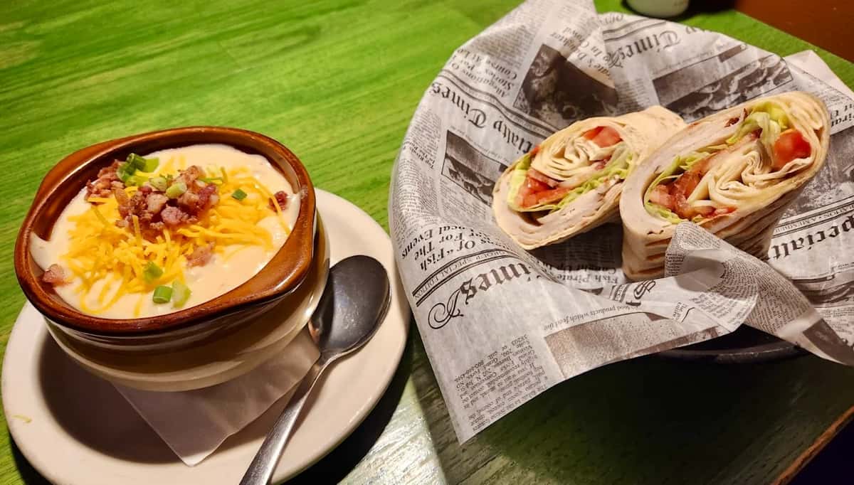 Creamy loaded potato soup topped with cheese and bacon, served with a turkey wrap filled with lettuce and tomato.