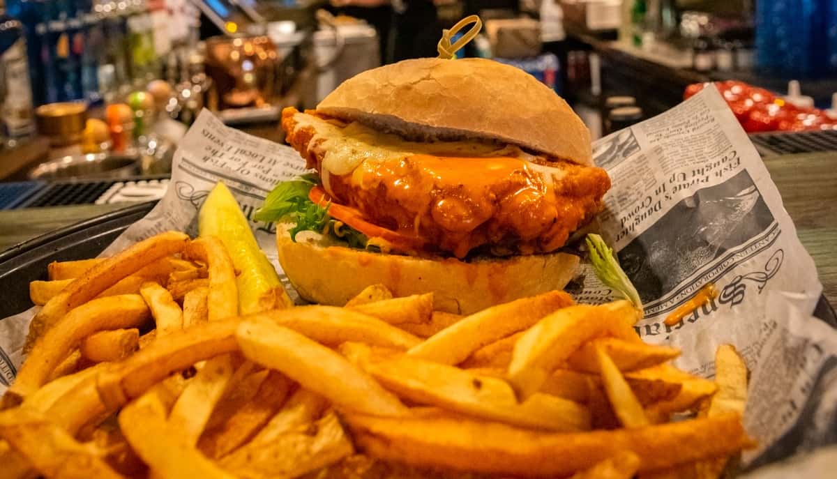 Buffalo chicken sandwich topped with melted cheese, lettuce, and tomato, served with fries and a pickle spear.