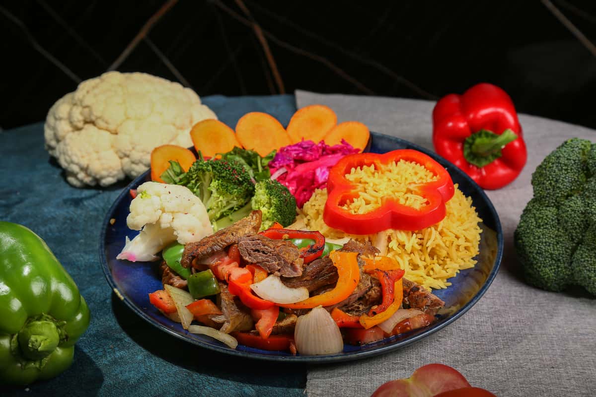 Vibrant Middle Eastern or Mediterranean rice plate with yellow basmati rice, sautéed beef strips, grilled bell peppers, and assorted fresh vegetables like broccoli, cauliflower, and carrots.