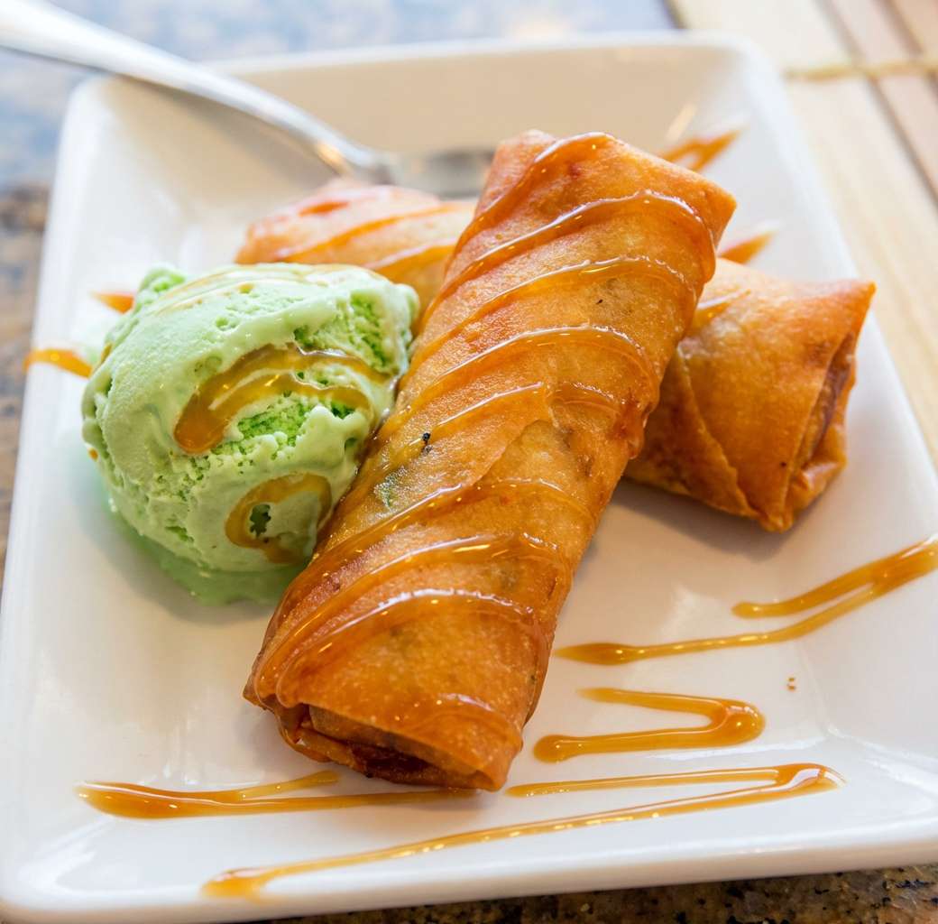 crispy golden spring rolls drizzled with sweet sauce, served with a scoop of green ice cream on the side for a sweet and crunchy dessert presentation.