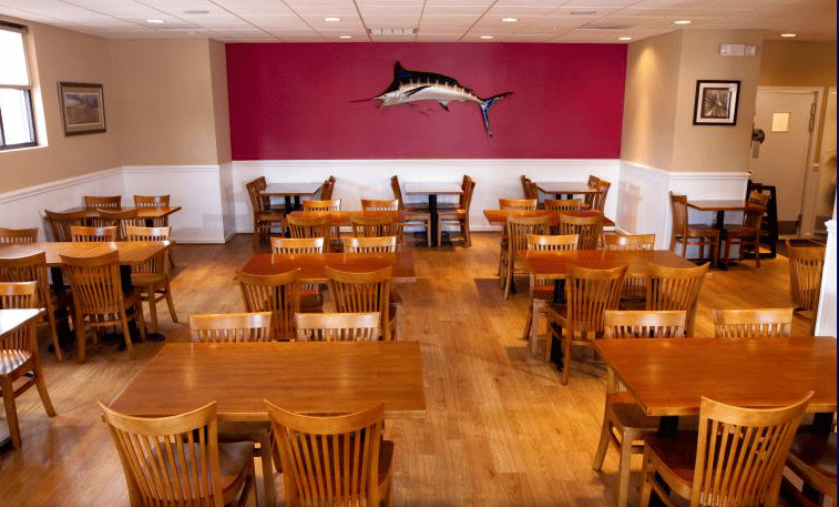 Dining room with brown wood tables and chairs. Mounted swordfish on red wall in background.