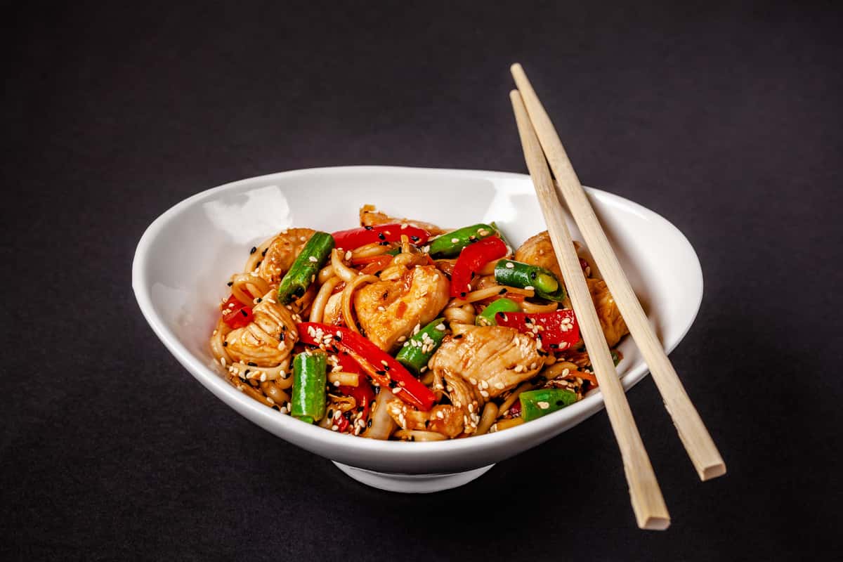 Bowl of stir-fried noodles with vegetables and chopsticks on the side.