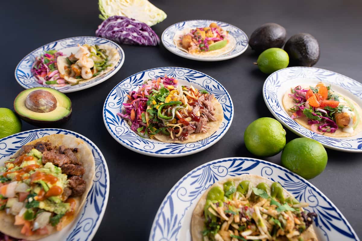 overhead spread of vibrant Mexican dishes including tacos, rice bowls, and fresh garnishes on a restaurant table