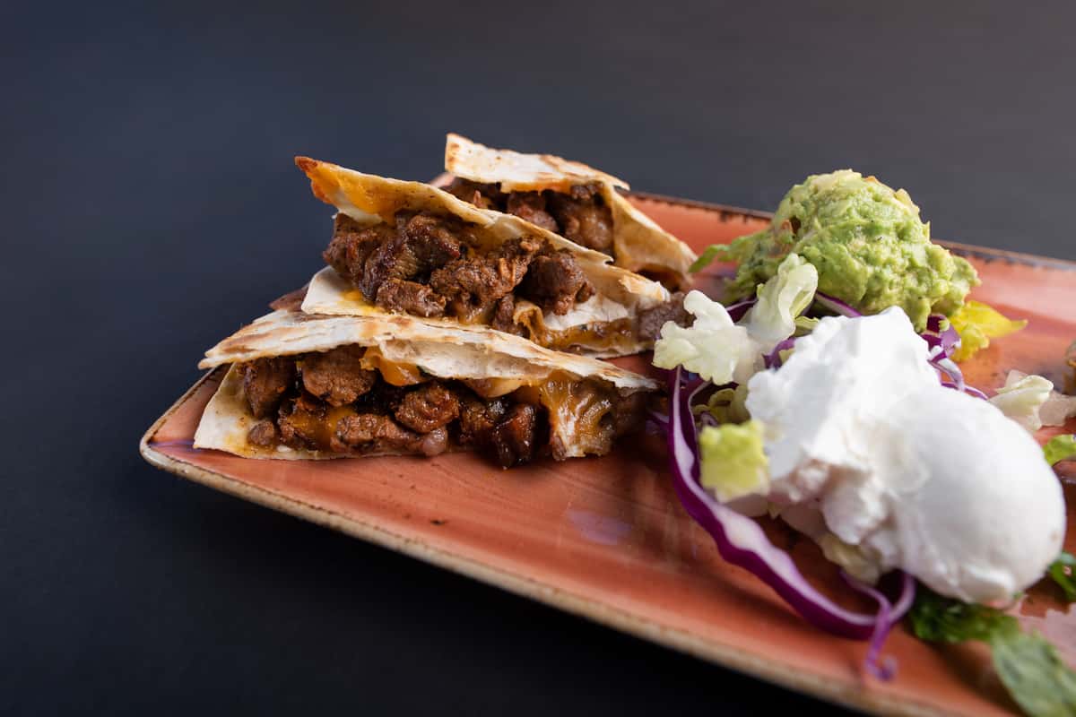 grilled quesadilla wedges filled with seasoned meat and melted cheese served with guacamole and sour cream