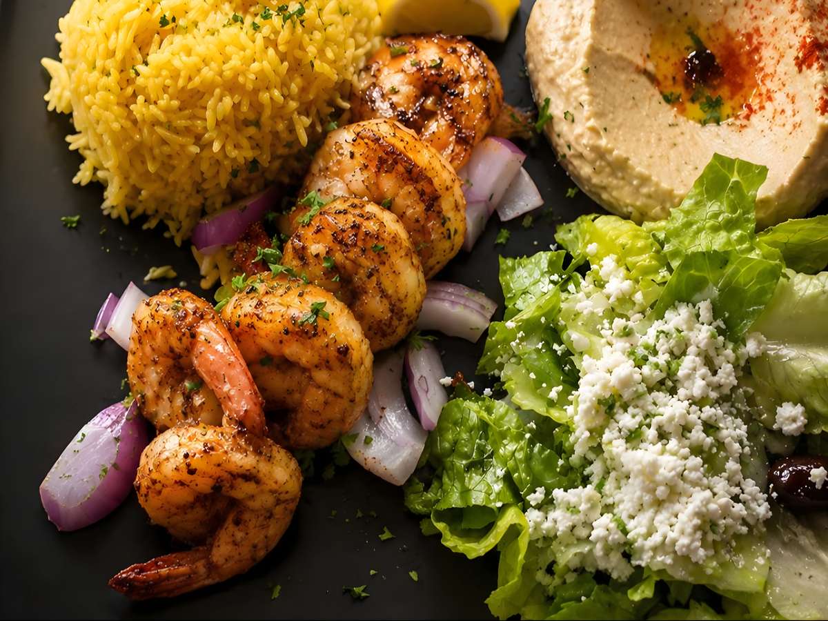 Grilled chicken skewers served with seasoned rice, hummus, and fresh salad.