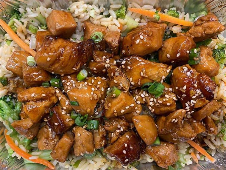 orange chicken over fried rice topped with sesame seeds and scallions