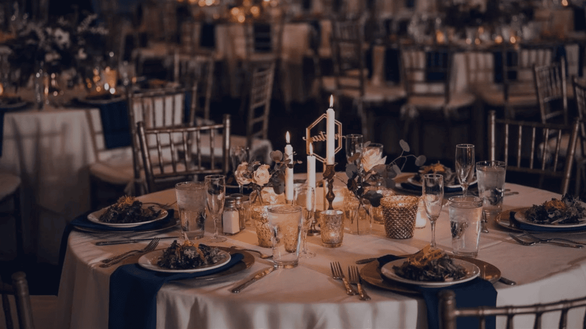 Elegant plated table with dark blue linens, white table cloth, and dimly lit with candles.