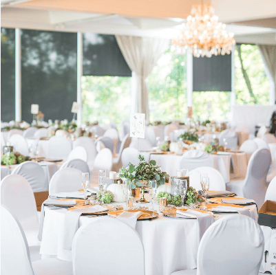 A refined wedding setting at the Buckeye Room in Columbus, Ohio, featuring tables adorned with white linens, gold cutlery, and natural greenery centerpieces. The soft glow of the chandeliers and daylight streaming through the draped windows create an inviting and romantic atmosphere for the special occasion." If you have more images, please continue to upload them, or let me know how else I may assist you.
