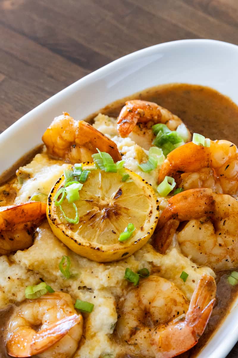 Southern shrimp and grits topped with grilled shrimp, charred lemon, green onions, and rich Cajun-style gravy in a white serving bowl