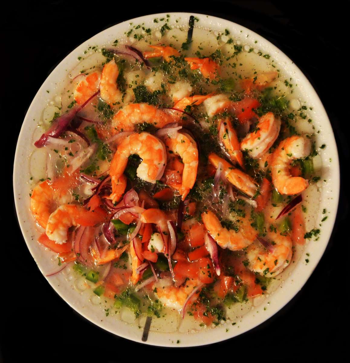 Colorful shrimp ceviche in citrus marinade, garnished with red onions, diced tomatoes, and chopped cilantro, served in a white bowl.
